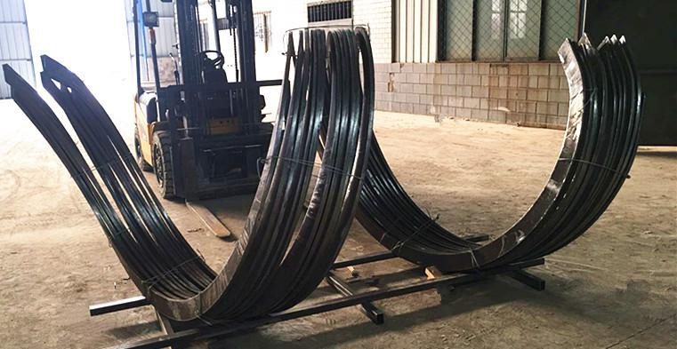 Stacks of curved metal beams are arranged in a warehouse