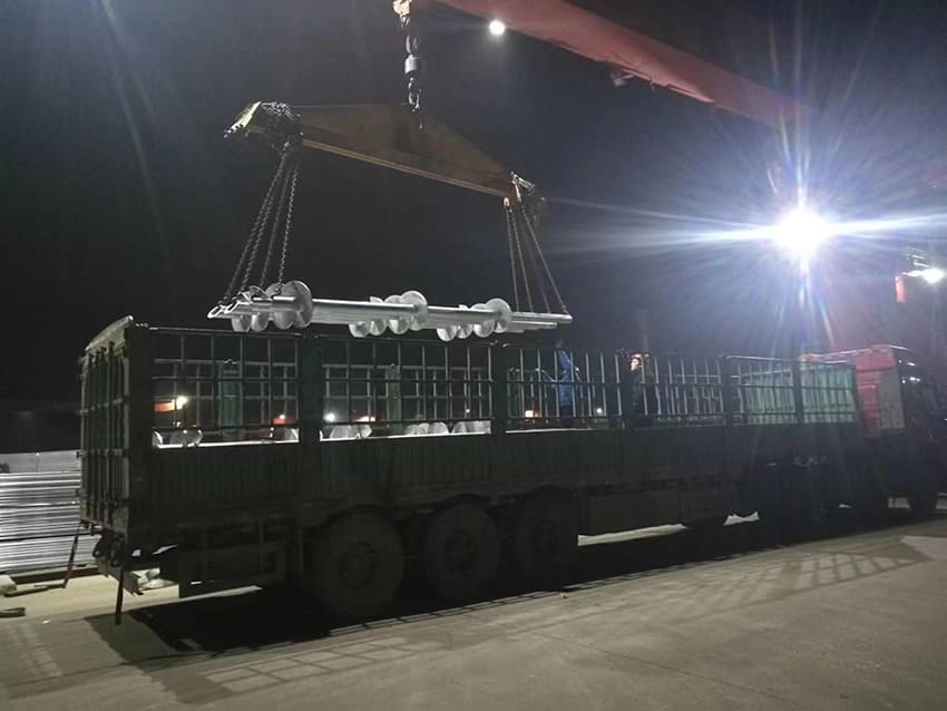 crane is loading long metal pipes onto a flatbed truck